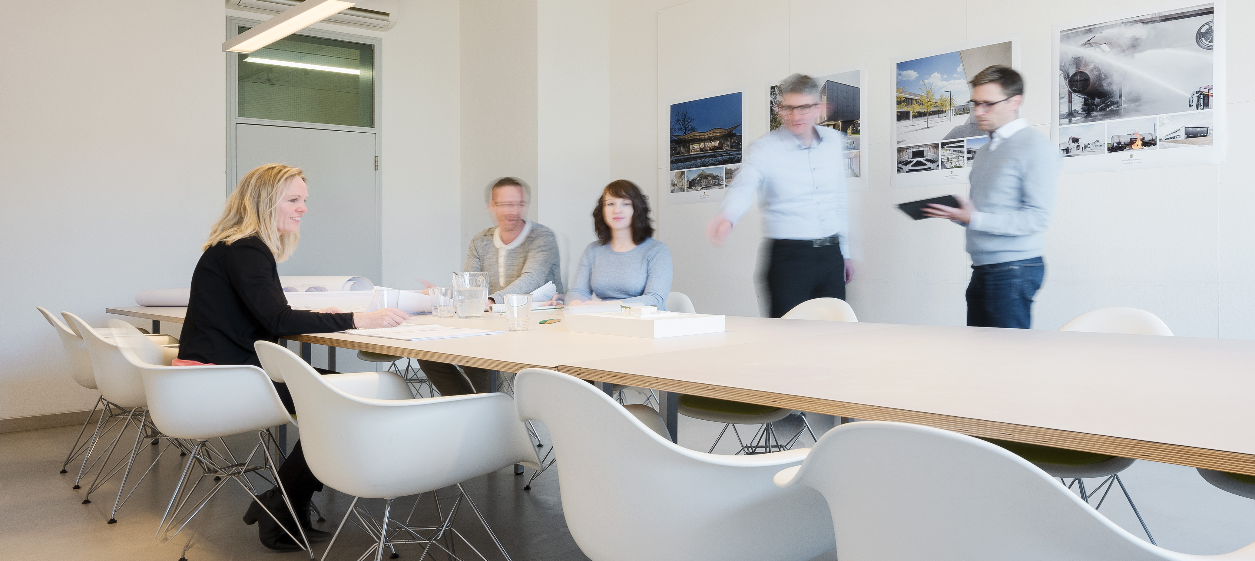 zwei Damen und drei Herren besprechen ein Architekturmodell auf einem Tisch in einem Besprechungsraum
