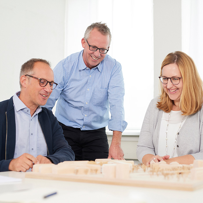 zwei Mitarbeiter und eine Mitarbeiter besprechen ein Architekturmodell am Tisch