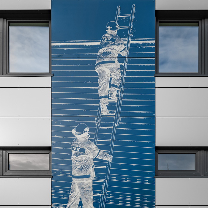 Ein Kunstwerk an der Fassade zeigt zwei THW Mitarbeitende, wie sie eine Leiter besteigen