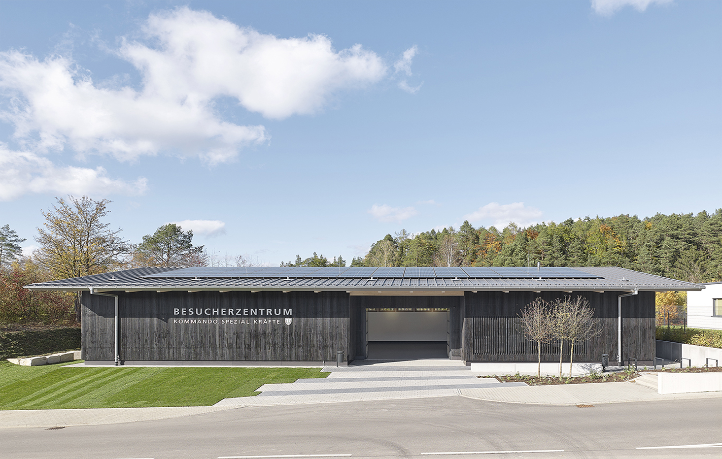 Das Besucherzentrum Kommando Spezialkräfte, ein langgestreckter einschössiger Holzbau mit Satteldach und dunkler Fassade  